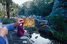 Holding a postcard of the painting in front of the scene